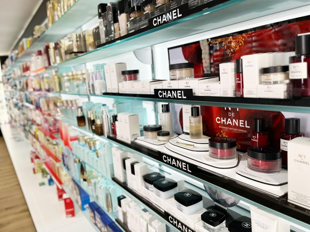 Beleuchtete Produktregale einer Parfümerie mit luxuriöser Hautpflege und Düften der Marke Chanel. Im Vordergrund steht die Serie N°1 de Chanel in weißen und roten Verpackungen, daneben verschiedene Pflegeprodukte und Parfums in eleganter Anordnung. Die hellen Regale und Spiegelrückwand betonen das hochwertige Ambiente.