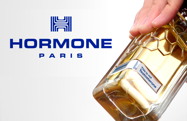 Zwei Hände halten futuristisch geformte Parfumflakons in warmen Gold- und Bernsteintönen vor hellem Hintergrund. In der Mitte steht das blaue Logo mit dem Schriftzug „HORMONE PARIS“. Auf den Etiketten der Flakons stehen Hinweise wie „This is not Dopamine“