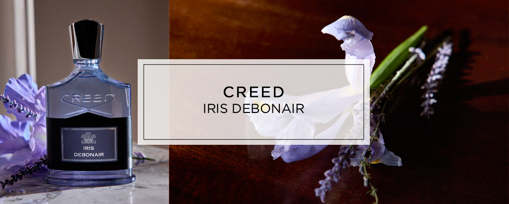 Creed Iris Debonair. Links steht der dunkelblaue Parfumflakon neben violetten Blüten. Rechts liegen weiße und violette Irisblüten auf dunklem Holz. In der Bildmitte steht der Schriftzug ‚CREED – IRIS DEBONAIR‘.
