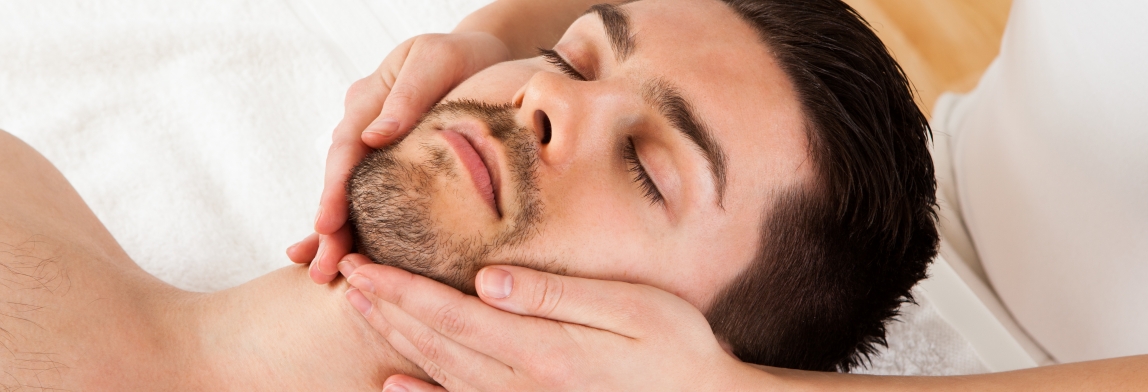 Entspannter Mann liegt auf einer Behandlungsliege und erhält eine kosmetische Gesichtsbehandlung mit sanfter Massage