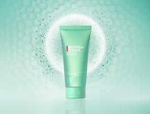 Ein grünes Biotherm Homme Körperpflegeprodukt (Duschgel oder Lotion) steht vor einem mintgrünen Hintergrund mit einem leuchtenden Ring aus Partikeln.