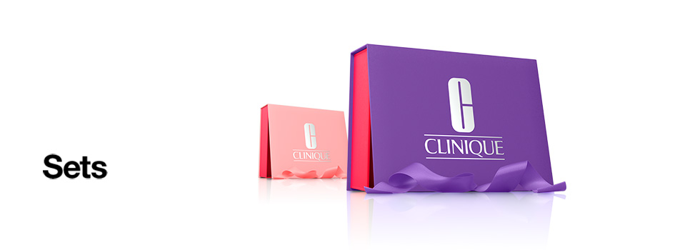 Zwei Geschenkboxen von Clinique, eine in Lila mit Schleife im Vordergrund und eine kleinere in Pink im Hintergrund, daneben der Text 'Sets' auf weißem Hintergrund.
