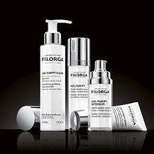 Vier Filorga Pflegeprodukte aus der AGE-PURIFY Serie in weiß-silberner Verpackung, auf einem glänzenden schwarzen Untergrund stehend. Enthalten sind ein Reinigungsgel mit Pumpspender, zwei Seren und eine Creme.