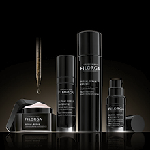 Vier Filorga Hautpflegeprodukte in eleganter schwarzer Verpackung vor dunklem Hintergrund. Abgebildet sind Creme, Serum, Lotion und Augenpflege aus der Global-Repair Linie, daneben eine Pipette mit einem Tropfen Serum.