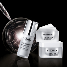 Filorga LIFT-DESIGNER Serumflasche und zwei Cremetiegel aus der Lift-Structure-Serie vor einem dunklen Hintergrund mit leuchtendem Glaseffekt. Links oben eine Pipette mit einem schimmernden Tropfen.