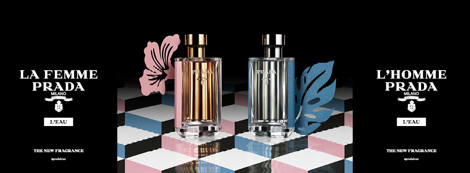 Werbung für Prada-Düfte: In der Mitte stehen zwei elegante Parfumflakons auf einem geometrischen Bodenmuster. Links der roségoldene Flakon 'La Femme Prada L’Eau' mit rosa Blütensilhouette, rechts der silberne Flakon 'L’Homme Prada L’Eau' mit blauer Blattsilhouette. Links und rechts auf schwarzem Hintergrund die Produktnamen und der Text 'The New Fragrance'.