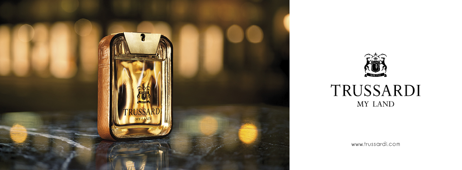 Werbung für Trussardi 'My Land': Links ein eleganter, goldfarbener Parfumflakon mit Lederdetails und Wappenlogo auf spiegelndem Marmortisch, im Hintergrund warme Lichter in Unschärfe. Rechts der Schriftzug 'TRUSSARDI MY LAND' mit Logo auf weißem Hintergrund.